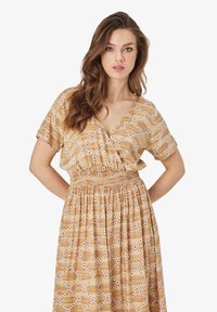 Rochie cu mânecă scurtă, decolteu în V, realizată dintr-un material bej cu un model geometric alb și talie smockată pentru o siluetă ajustată. Design de lungime medie.