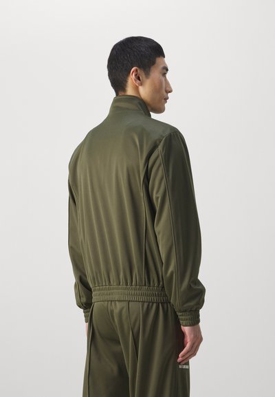 Ελιάς πράσινη ζακέτα προπόνησης με υψηλό γιακά, ελαστική μέση και ριμπά μανσέτες. Λείο ύφασμα, μινιμαλιστικός σχεδιασμός, χωρίς ορατά σχέδια.