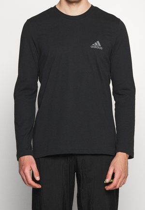 Zwarte longsleeve t-shirt van katoen met een ronde halslijn en een subtiele grijze Adidas-logo op de linkerborst. Zachte textuur.