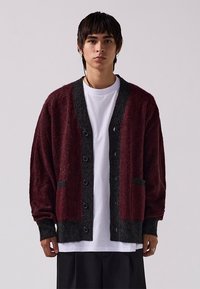 Burgundská a tmavošedá prešívaná cardigan s voľným strihom vyrobená z mäkkej látky, s gombíkmi, dvoma prednými vreckami a rebrovanými manžetami a lemom.