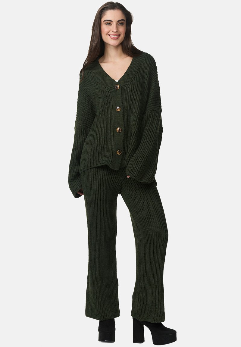 Grön stickad cardigan med V-ringning och oversized passform, med stora bruna knappar och matchande högmidjade stickade byxor. Svarta platåskor.