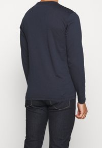 Granatowa koszula z długim rękawem wykonana z miękkiej bawełny. Posiada okrągły dekolt, prosty dół, gładką fakturę oraz minimalistyczny design bez widocznych logo.