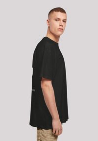 Zwarte katoenen t-shirt, korte mouwen, losse pasvorm. Voorkant met een grafisch ontwerp; achterkant bevat tekst. Casual stijl, zachte textuur.
