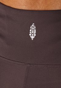 Dark brown stretchy fabric waistband with a white floral logo printed at the center, featuring smooth texture and subtle stitching details.