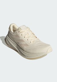 Beige hardloopschoen met een bovenwerk van mesh, een gestructureerd patroon, een design met drie strepen en een gevoerde zool met een lichte verhoging bij de hak.