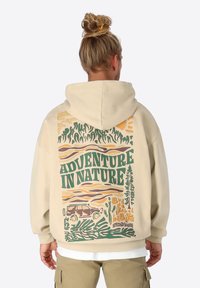 Beige Kapuzenpullover mit einem großen Grafikmotiv auf der Rückseite, das den Text "ABENTEUER IN DER NATUR" zeigt und Bäume, Wellen und ein Auto in erdigen Farben abbildet.