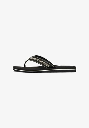 Schwarze Flip-Flops mit einem strukturierten Riemen, der das "TOMMY HILFIGER"-Logo zeigt, einem weißen Akzentstreifen auf der Sohle und einer glatten Fußbett.