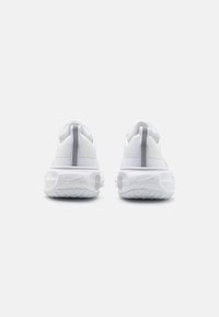 Witte sportieve schoenen met een gestructureerde bovenkant, voorzien van een gewatteerde kraag en een grijs Nike-logo op de hiel, afgeronde zool en een trekstrip.