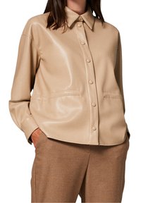 Chemise beige brillante à boutons avec col, dotée de deux poches avant et d'une coupe décontractée, assortie à un pantalon marron.