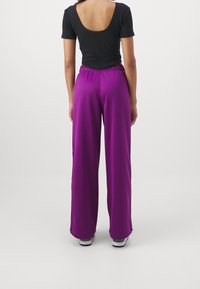 Black fitted top with a scoop back, paired with loose, flowy magenta pants featuring an elastic waistband and a smooth texture.