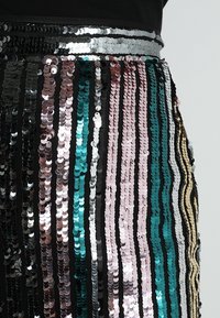 Jupe pailletée avec des rayures verticales en noir, bleu-vert, rose, argent et bronze ; texture scintillante avec des tailles de paillettes variées et une taille lisse.
