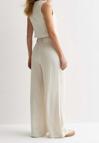 Ensemble beige clair en deux pièces comprenant un haut sans manches et un pantalon large avec de subtiles rayures verticales, fabriqué à partir d'un tissu texturé.