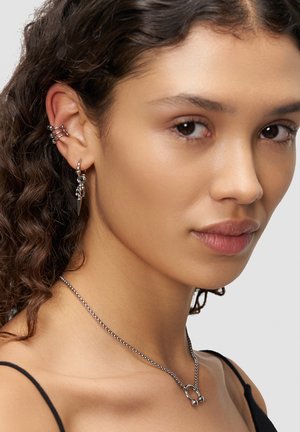 Silver jewelry features multiple earring styles: a triple hoop and a dangling spike. A thin chain necklace adds a minimalistic touch.