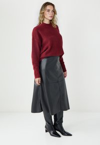 Bordeaux gebreide trui met ribbelmanchetten, gecombineerd met een zwarte leren midi-rok, benadrukt door puntige zwarte haklaarzen.