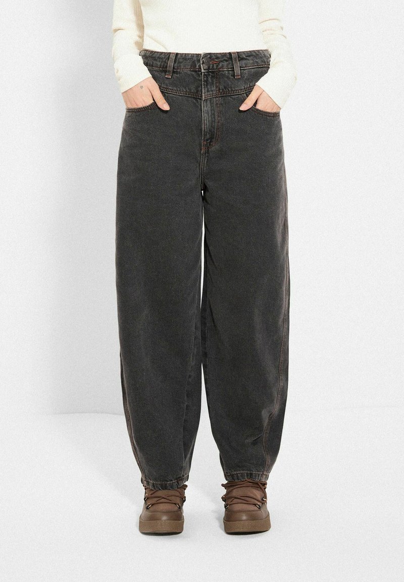 Luźne czarne dżinsy z wysokim stanem, z przednimi kieszeniami i kontrastowym szwem, zestawione z brązowymi butami na sznurówki.