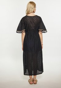 Rochie maxi din dantelă neagră cu mâneci scurte, talie ajustabilă cu șnur și accente cu ciucuri la mâneci. Textură transparentă cu modele în formă de diamant.
