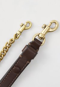 Zwei goldene Drehmünzsnaps, die an einer goldenen Kette und einem braunen Lederband mit Nähten und einem Knopf befestigt sind.