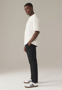 Weißes Kurzarmhemd, schwarze Slim-Fit-Hosen und weiße Sneaker mit schwarzen Streifen. Glatte Stoffqualität mit lockerer Passform und minimalistischem Design.