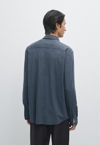 Camicia a maniche lunghe in tessuto blu scuro, con colletto a punta, cucitura della spalla sul retro e polsini con bottoni. Texture morbida e vestibilità comoda.