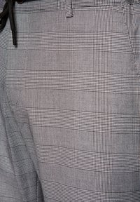 Szare spodnie w kratę z teksturowanej tkaniny w wzór kratki. Projekt zawiera małe kwadraty w odcieniach czerni i bieli oraz detal w pasie.