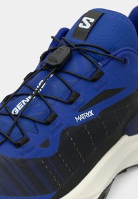 Sapato atlético azul e preto com sistema de atacadores rápidos pretos, texto branco "MATRIX" e "GENERATION", e sola acolchoada branca.