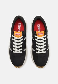 Schwarze Sportschuhe mit weißen Streifen, obermaterial aus strukturiertem Stoff, weiße Schnürsenkel, Gummigummi-Außensohle und rote Einlegesohlen mit "CAMPER"-Logo.