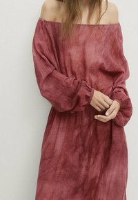 Robe longue décolletée en tissu bordeaux délavé, avec de longues manches à poignets froncés et une silhouette ample et fluide.