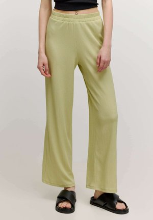 Helle grüne weit geschnittene Hose aus strukturiertem Stoff, mit einem elastischen Bund. Kombiniert mit schwarzen Riemensandalen.