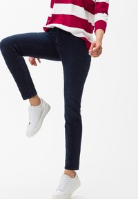 Jeans de mezclilla azul oscuro con un ajuste slim y detalles en los bolsillos, combinados con zapatillas blancas y una blusa a rayas rojas y blancas.
