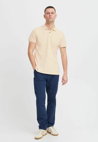 Beige polo-skjorte med korte ermer, flatstrikket krage, to-knapp placket, kombinert med marineblå bukser og hvite sneakers.