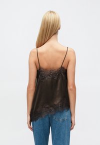 Satin camisol in chocoladebruin met kantafwerking, dunne verstelbare bandjes en een vloeiend ontwerp, gezien van achteren gedragen met een spijkerbroek.