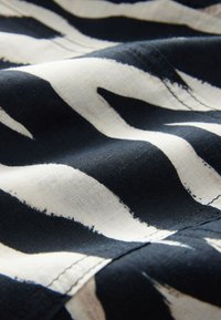 Black and white fabric with abstract zebra-like stripes and visible stitching along the seams.