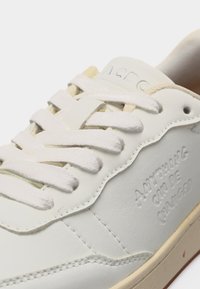 Baskets en cuir blanc avec lacets blancs, texte embossé "AMORAVING CALM DE CHARGER" sur le côté, et semelle beige clair visible.