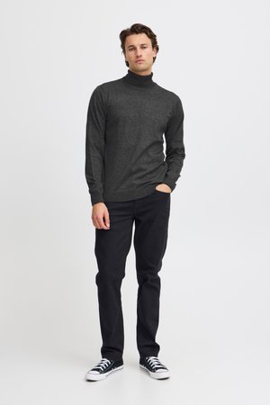 Mørkegrå genser med høy krage og tettsittende design, laget av teksturert stoff. Kombinert med svarte bukser og svarte joggesko.