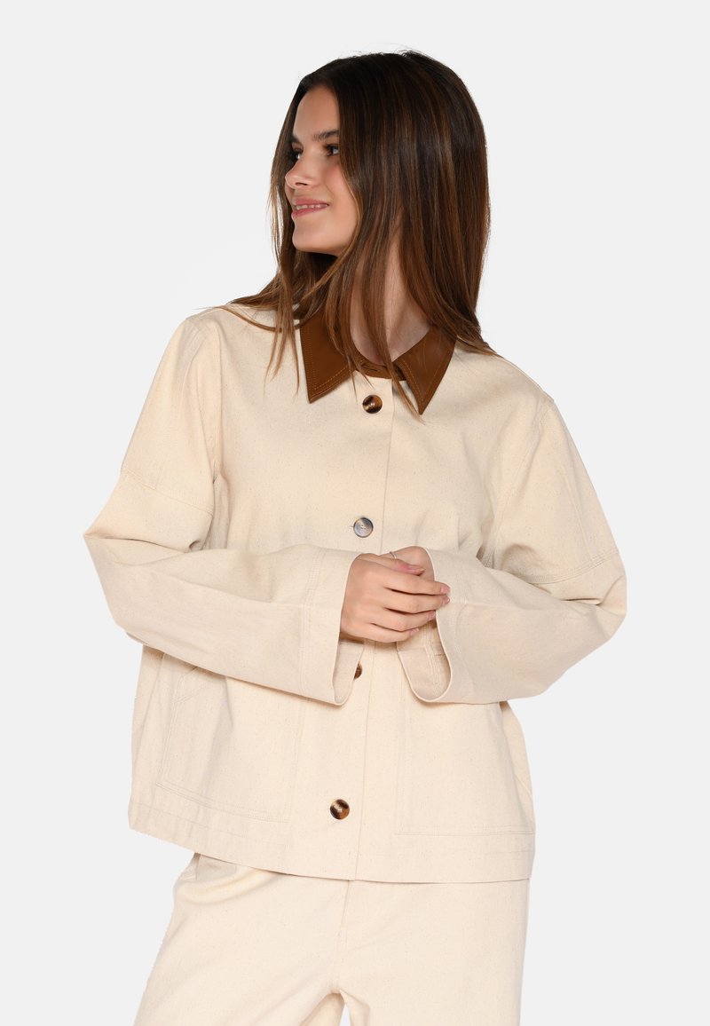 Crème-kleurige jas van gestructureerde stof, met een leren kraag in bruin en oversized knopen. Wijde mouwen en een relaxed fit.