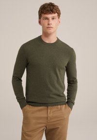 Olíva zöld kötött pulóver kerek nyakkal és bordázott mandzsettákkal, világosbarna nadrággal párosítva. Puha textúra és testhezálló fazon.