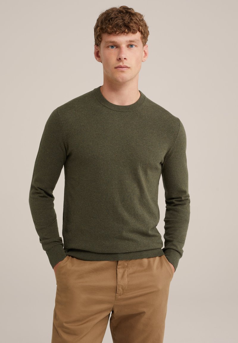 Olíva zöld kötött pulóver kerek nyakkal és bordázott mandzsettákkal, világosbarna nadrággal párosítva. Puha textúra és testhezálló fazon.