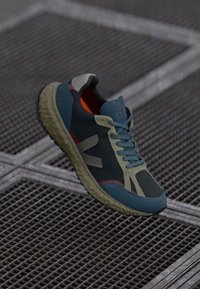Adidași sport cu o suprafață din plasă de un albastru închis, accente verzi și o talpă din cauciuc texturată. Oferă un sistem dinamic de șireturi și un interior vibrant de culoare portocalie.
