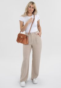 Borsa in pelle tan con hardware dorato, abbinata a pantaloni larghi in lino beige e a una t-shirt attillata bianca. Sneakers bianche completano il look.