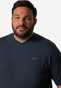 Tmavě modré tričko s výstřihem do V vyrobené z texturované látky, s jemným logem v levém horním rohu. Krátké rukávy, volný střih.