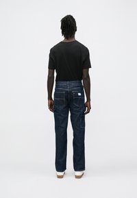 Mørkeblå jeans i denim med rett passform, kontrastsøm, baklommer og en logo-lapp på linningen. Sort t-skjorte synlig på toppen.