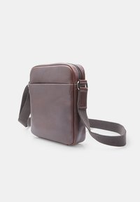 Hnědá kožená taška na rameno obdélníkového tvaru, hladké textury, se zapínáním na zip a nastavitelným textilním popruhem. Jednoduchý, funkční design.