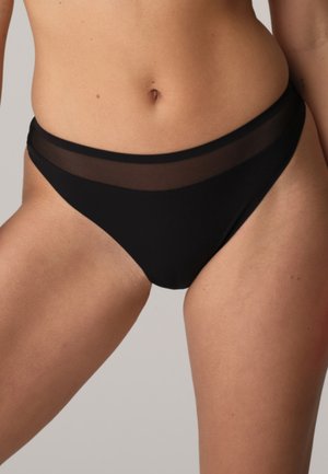 Donna che indossa un bikini nero con una fascia in rete trasparente, mostrata dalla metà del busto fino alla parte superiore delle cosce.