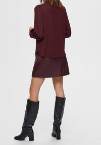 Burgundy blouse with puff sleeves, paired with a burgundy leather mini skirt. Black knee-high leather boots with block heels complete the outfit.