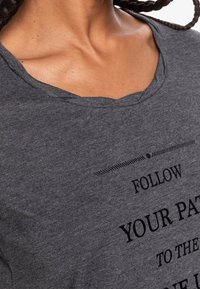 Camiseta de algodón gris con un escote amplio, mangas cortas y un diseño de texto impreso en negro que dice "SIGUE TU CAMINO HACIA EL..."