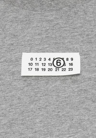 Szürke textíliára varrt fehér anyagcímke, amelyen fekete számok 0-tól 23-ig láthatók, a hatos szám feketével bekarikázva.