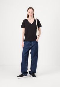 Black V-neck T-shirt paired with loose-fitting blue denim jeans. Model wears black sneakers and a small off-white handbag.