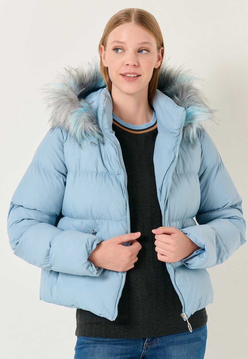Giacca puffer azzurro chiaro con cappuccio in pelliccia sintetica, chiusura con zip e polsini a coste. Presenta un design trapuntato e tasche laterali.