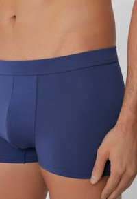 Námorně modré trenýrky vyrobené z hladkého, elastického materiálu s měkkým pasem a přiléhavým střihem, bez viditelných vzorů nebo akcentů.