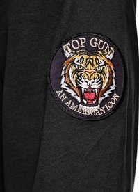 Czarna tkanina z okrągłą naszywką wyszywaną, przedstawiającą ryczącego tygrysa oraz napisem "TOP GUN AMERICAN ICON" na białym tle.